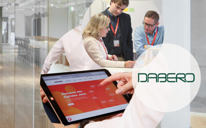 Das Bild zeigt valantic Mitarbeiter bei einer Besprechung, ein Logo der Firma Dabero sowie ein Tablet.