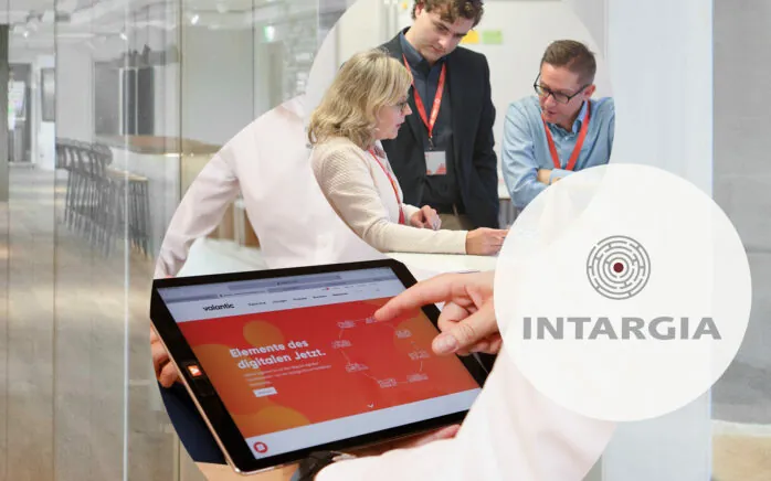 Das Foto zeigt das Logo der Managementberatung Intargia, die sich valantic angeschlossen haben, sowie valantic Mitarbeiter im Meeting und ein Tablet.