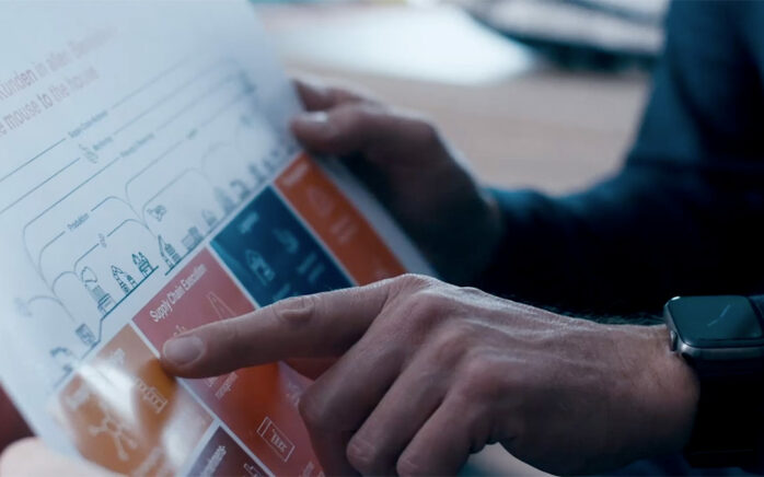 Image shows a scene from the valantic image film: a finger of a man pointing at an infographic