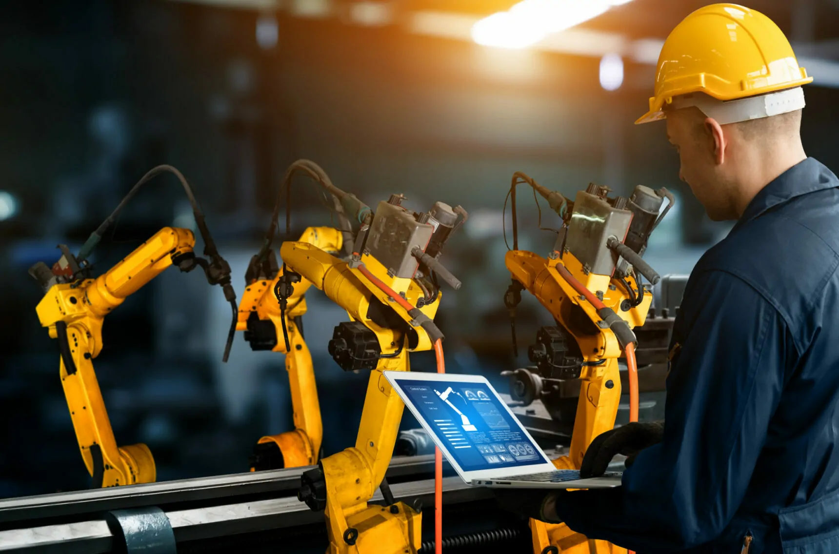 Bild eines Roboterarms, der von einem Mann mit Laptop gesteuert wird, Trend in der Automotive-Industrie: Smart Industries