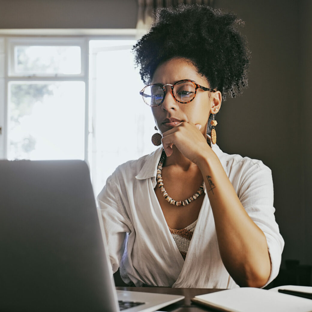 Woman thinking, planning, online research and brainstorming ideas on her laptop