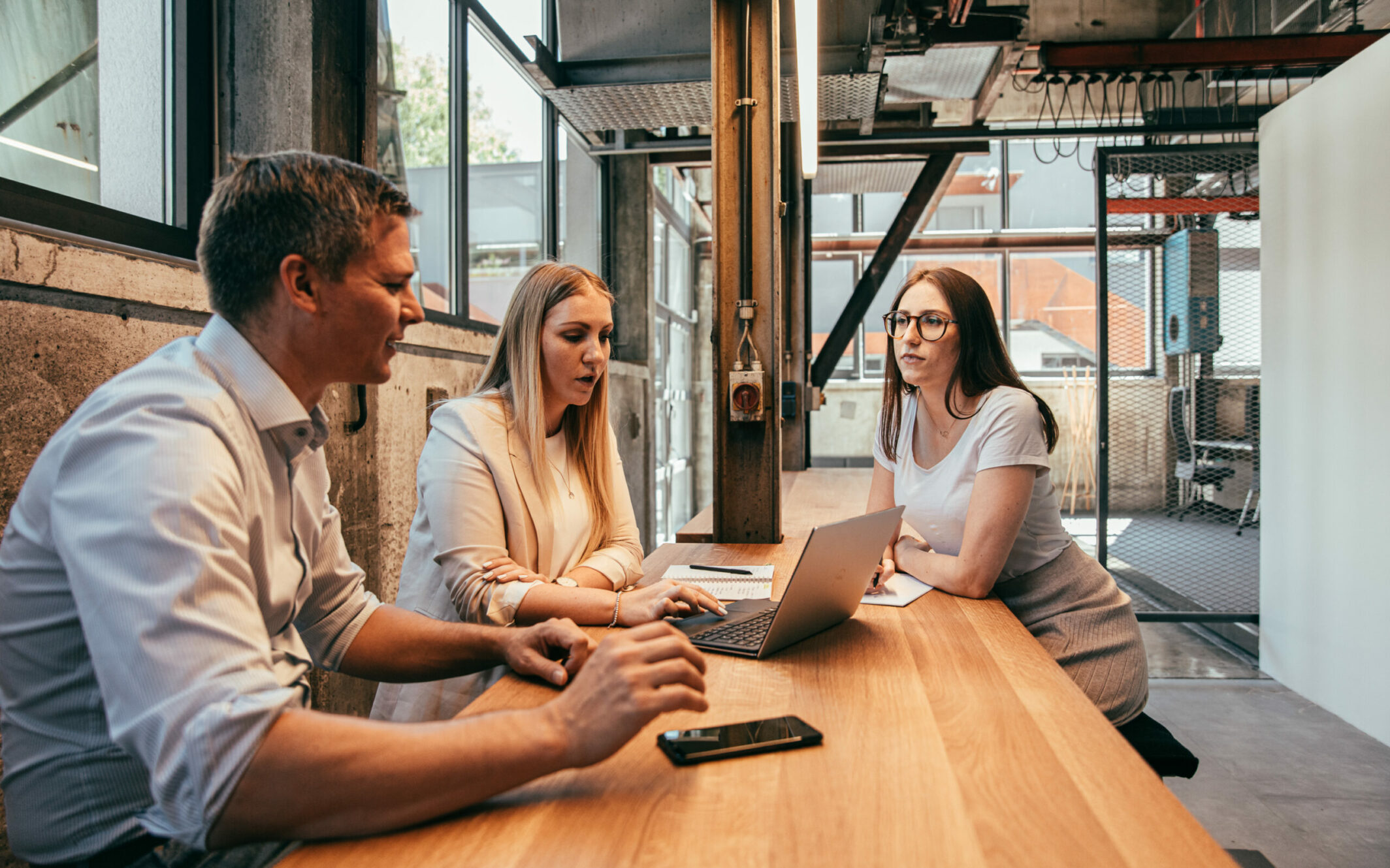 Drei valantic-Mitarbeiterinnen sitzen an einem hohen Holztisch und erarbeiten eine Digitale Transformationsberatung.