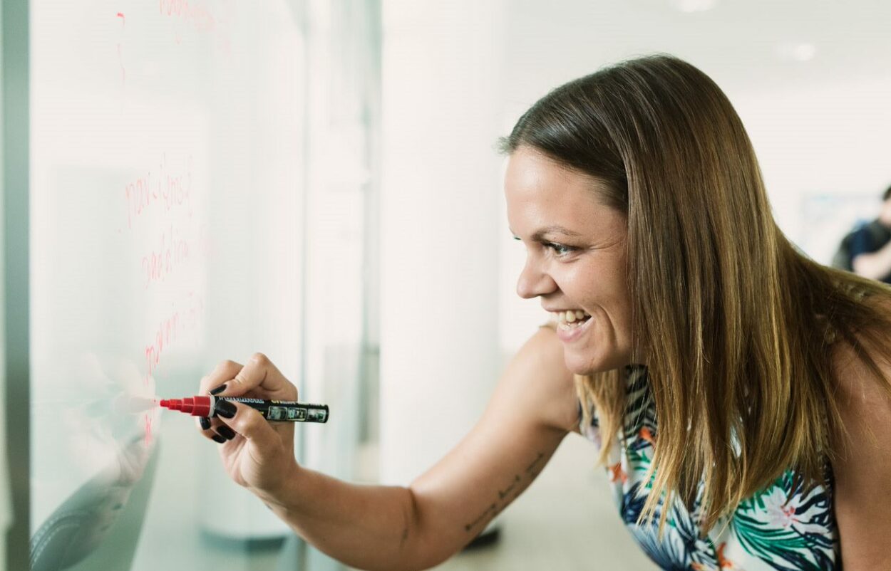 lächelnde Frau schreibt etwas mit rotem Stift auf ein Whiteboard