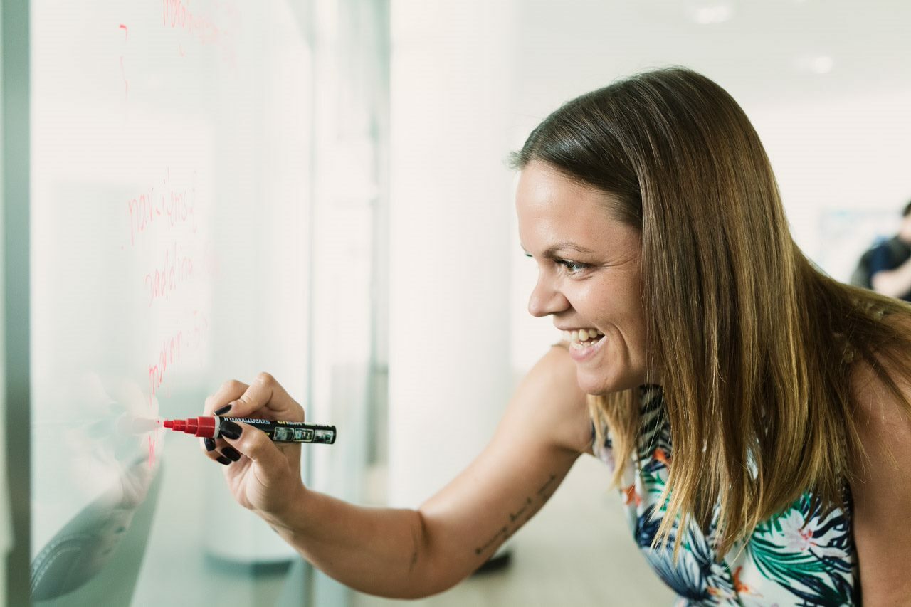 lächelnde Frau schreibt etwas mit rotem Stift auf ein Whiteboard