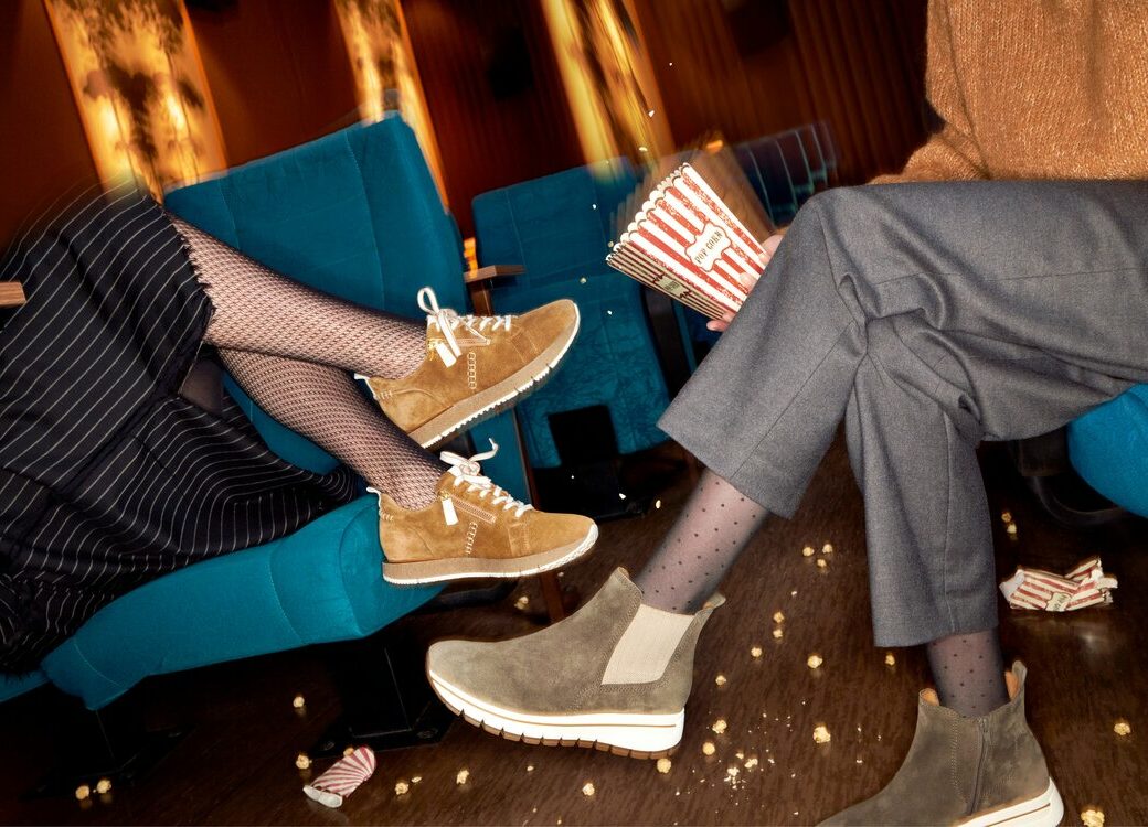 zwei Frauen sitzen in einer Bar und haben Popcorn in der Hand. Sie tragen beide eine Strumpfhose und Sneaker.