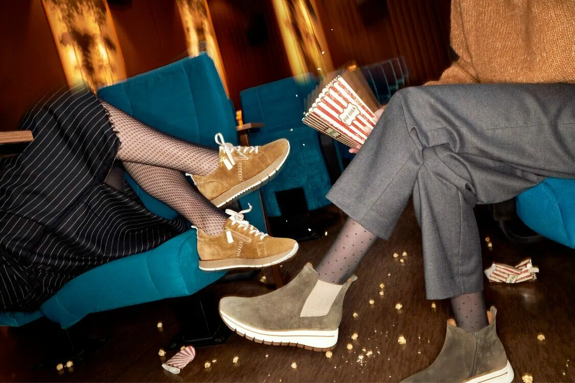 zwei Frauen sitzen in einer Bar und haben Popcorn in der Hand. Sie tragen beide eine Strumpfhose und Sneaker.