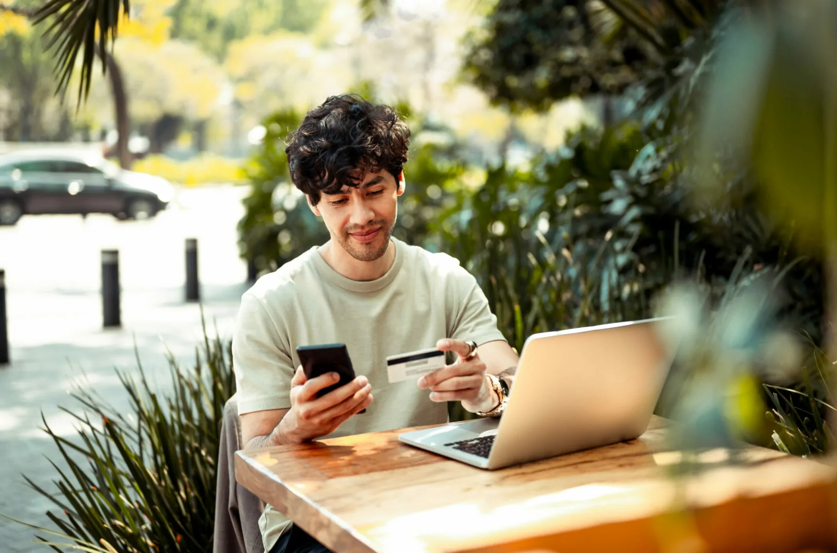 Bild von einem jungen Mann, der im Café mit Laptop sitzt und eine Kreditkarte in der Hand hält, SCM & Logistik