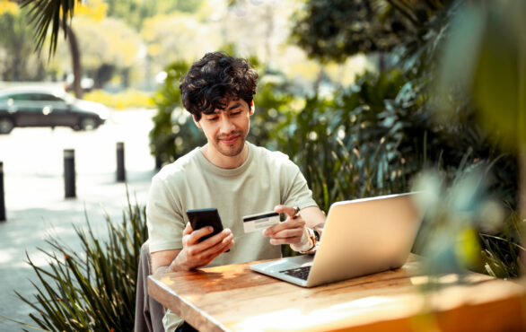 Bild von einem jungen Mann, der im Café mit Laptop sitzt und eine Kreditkarte in der Hand hält, SCM & Logistik