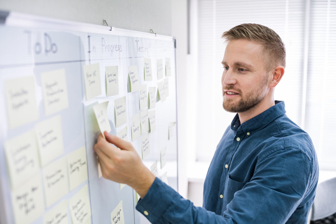 Mann schiebt gelbe Zettel an Whiteboard - effizientes Arbeiten im Team mit Low-Code-Plattformen