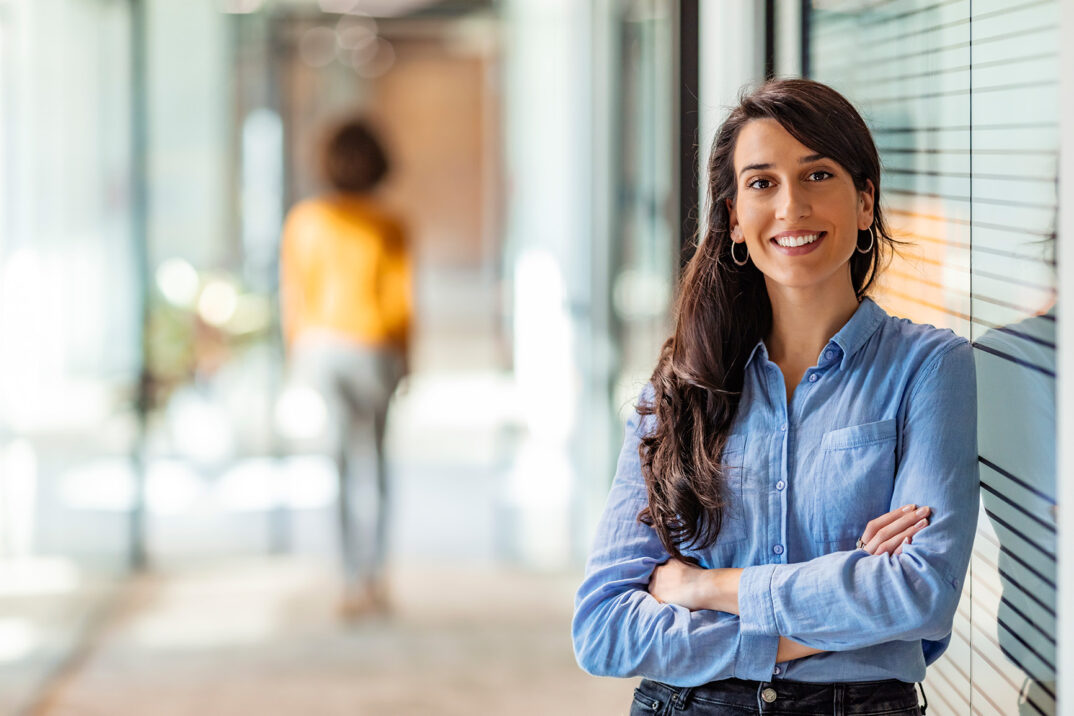 Lächelnde Frau im blauen Hemd angelehnt an eine Glaswand | Success Story Visana Micro Strategy Steigerung Produktivität im Vertrieb