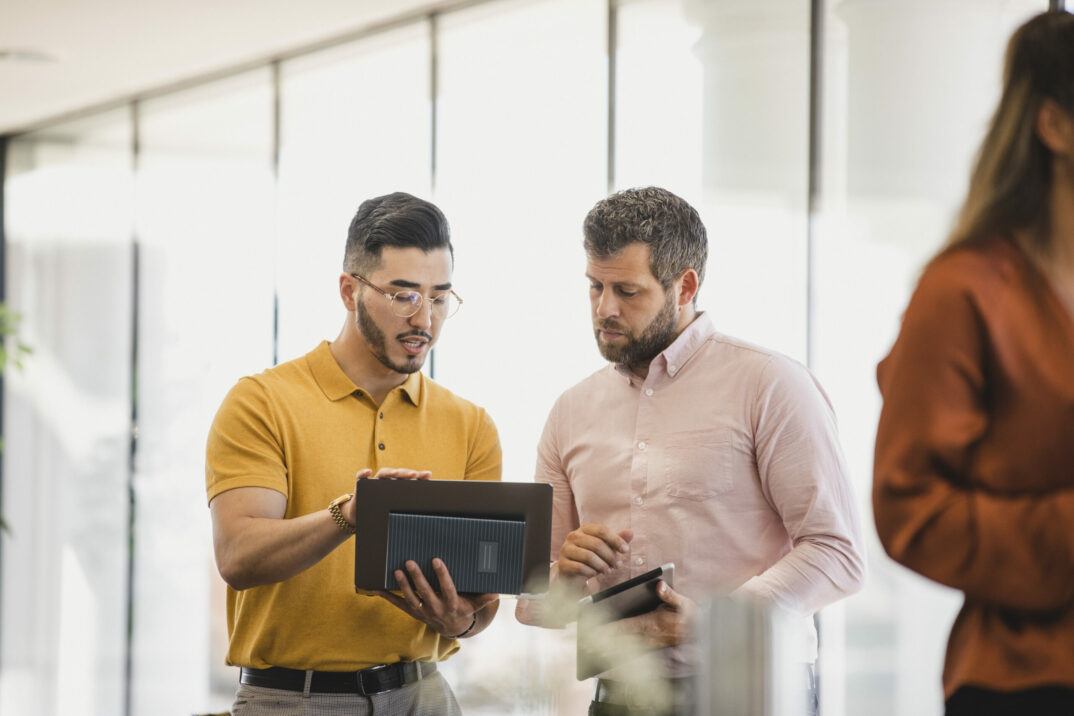 Hipster man holding laptop and explaining to coworker, support, guidance, advice