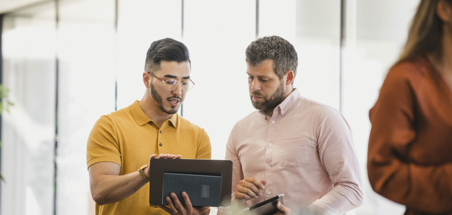 Hipster man holding laptop and explaining to coworker, support, guidance, advice