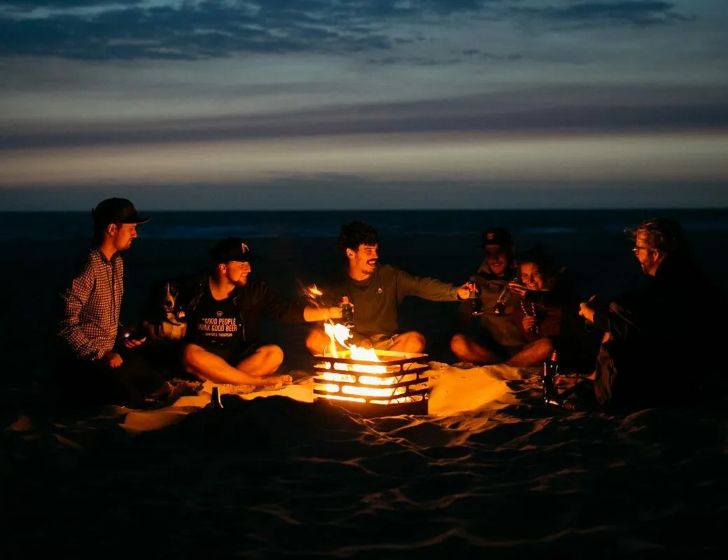 Eine Gruppe junger Leute sitzt bei Sonnenuntergang am Lagerfeuer mit dem Feuerkorb Cube von höfats.