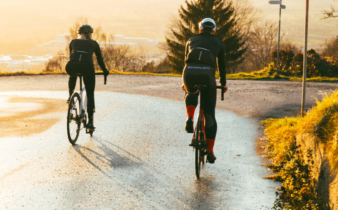 Photo of two cyclists from behind riding on a wet road.