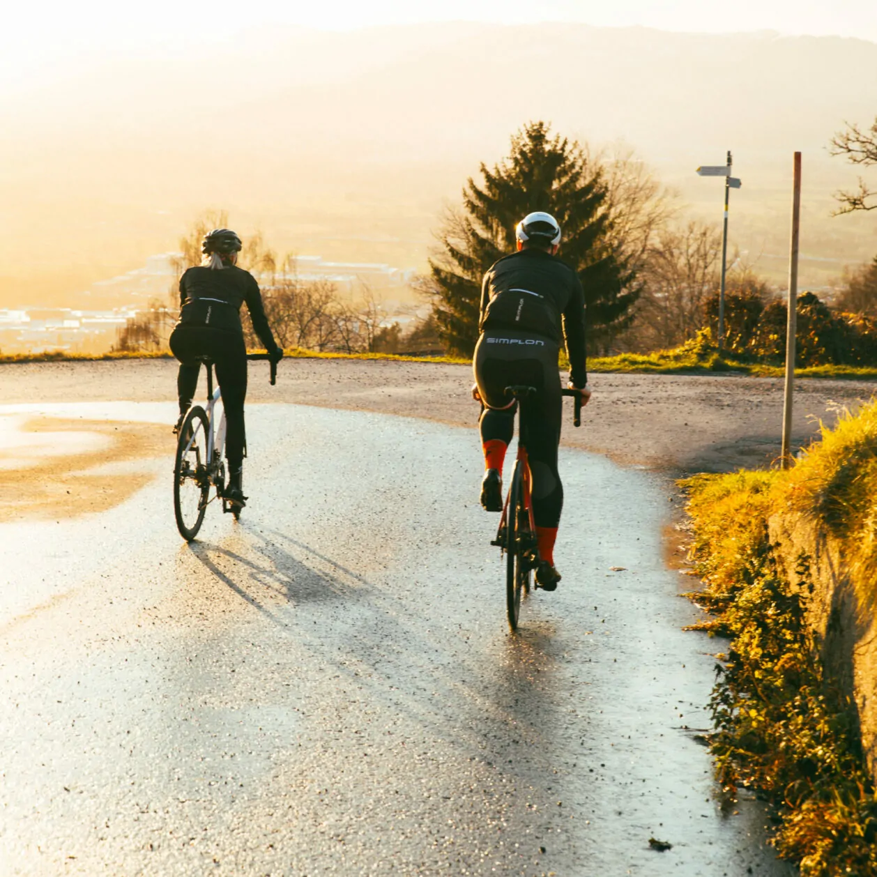 Photo of two cyclists from behind riding on a wet road.