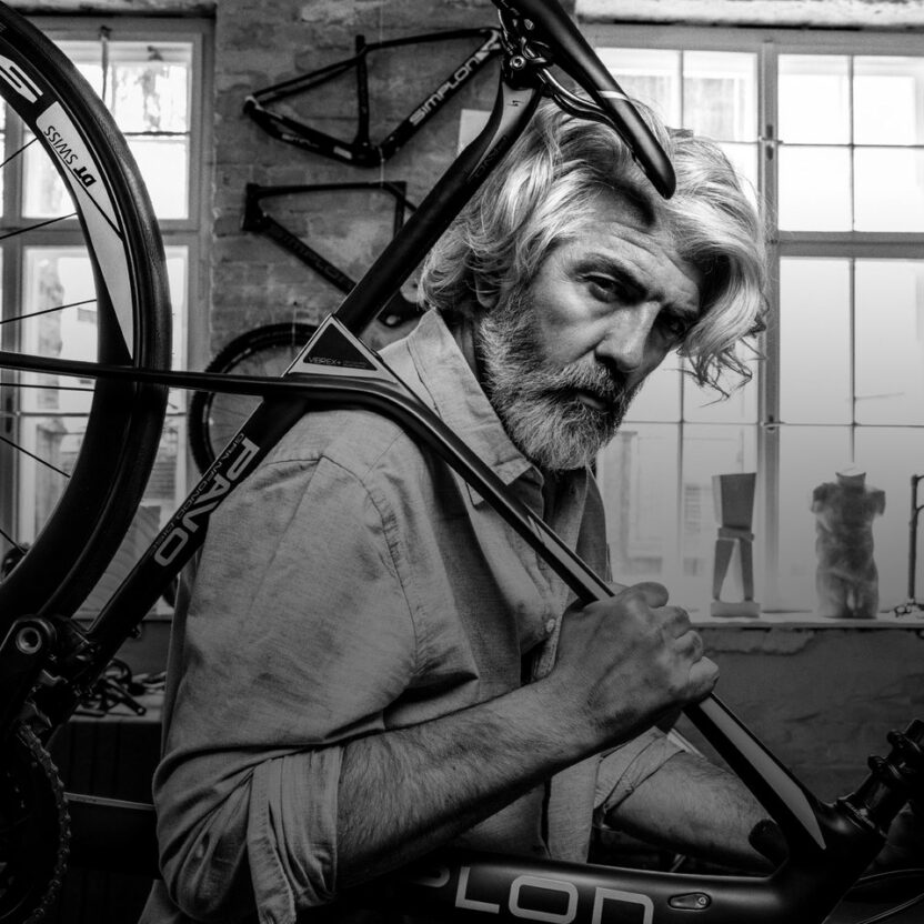 Picture of an elderly gentleman in a bicycle repair shop shouldering a SIMPON bicycle.