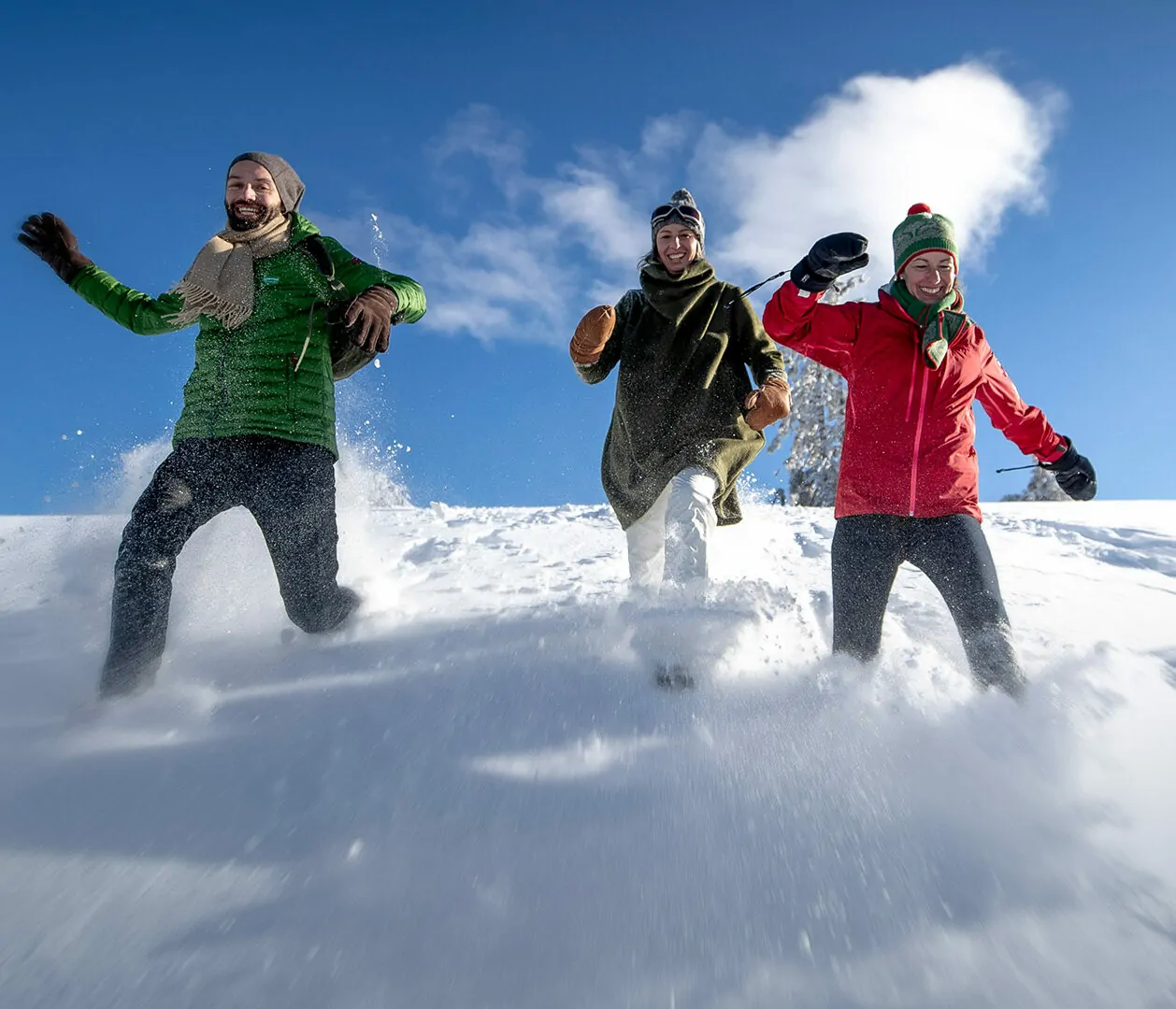Foto von drei Freundinnen, die einen beschneiten Hügel hinunterlaufen und dabei Spaß haben.