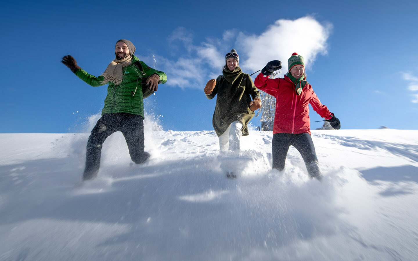 Foto von drei Freundinnen, die einen beschneiten Hügel hinunterlaufen und dabei Spaß haben.