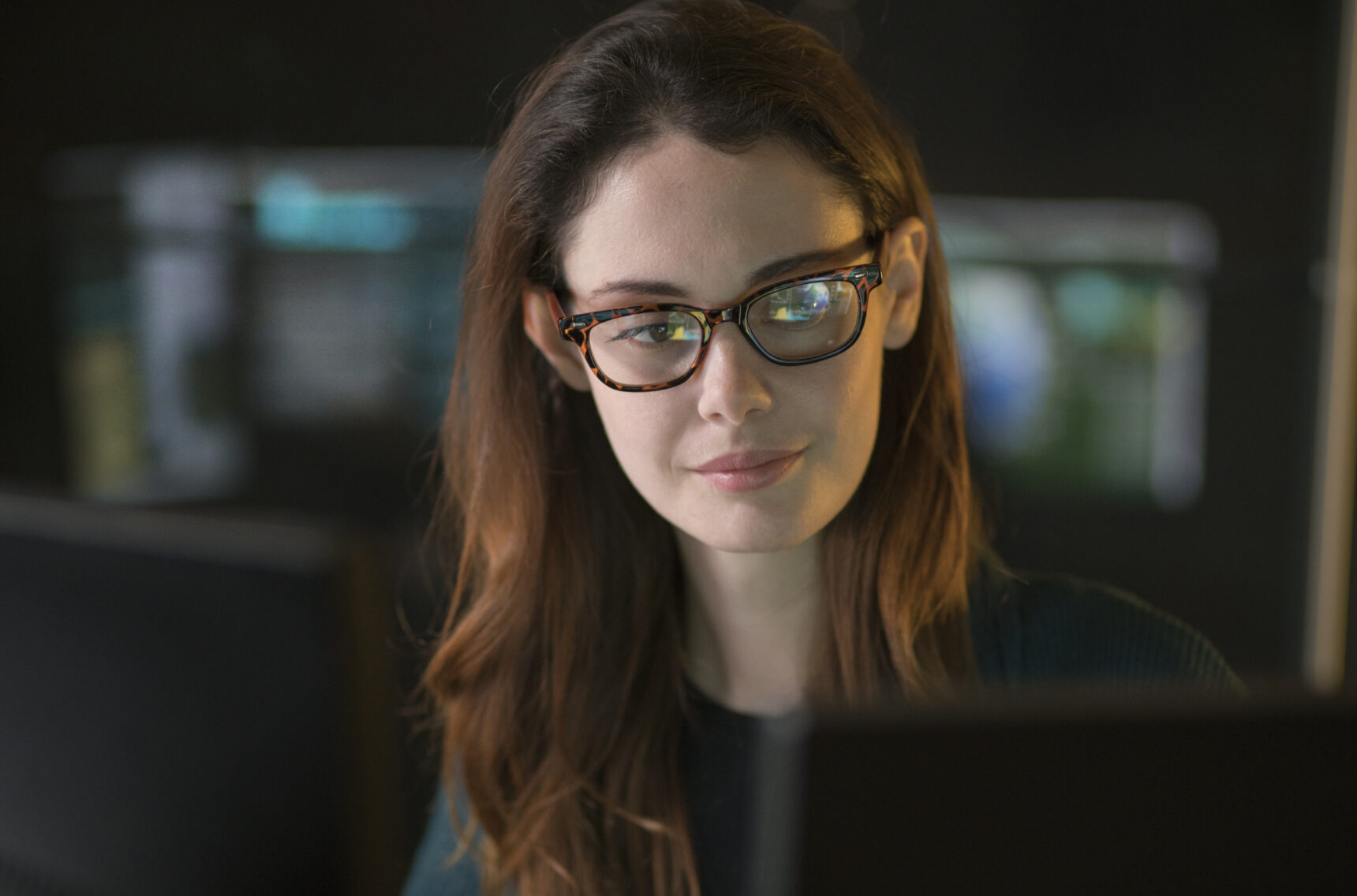 Bild von einer Frau, die in einem dunklen Büro über den Inhalt eines Computerbildschirms nachdenkt | Cyber Security: Wie sicher ist Ihre Unternehmens-IT? | Lünendonk