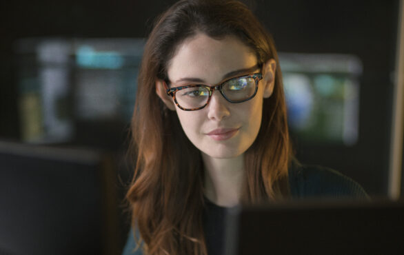 Bild von einer Frau, die in einem dunklen Büro über den Inhalt eines Computerbildschirms nachdenkt | Cyber Security: Wie sicher ist Ihre Unternehmens-IT? | Lünendonk