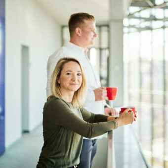 A man and a woman having a cup of coffee on their office balcony.