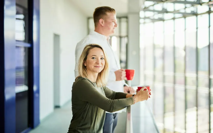 A man and a woman having a cup of coffee on their office balcony.