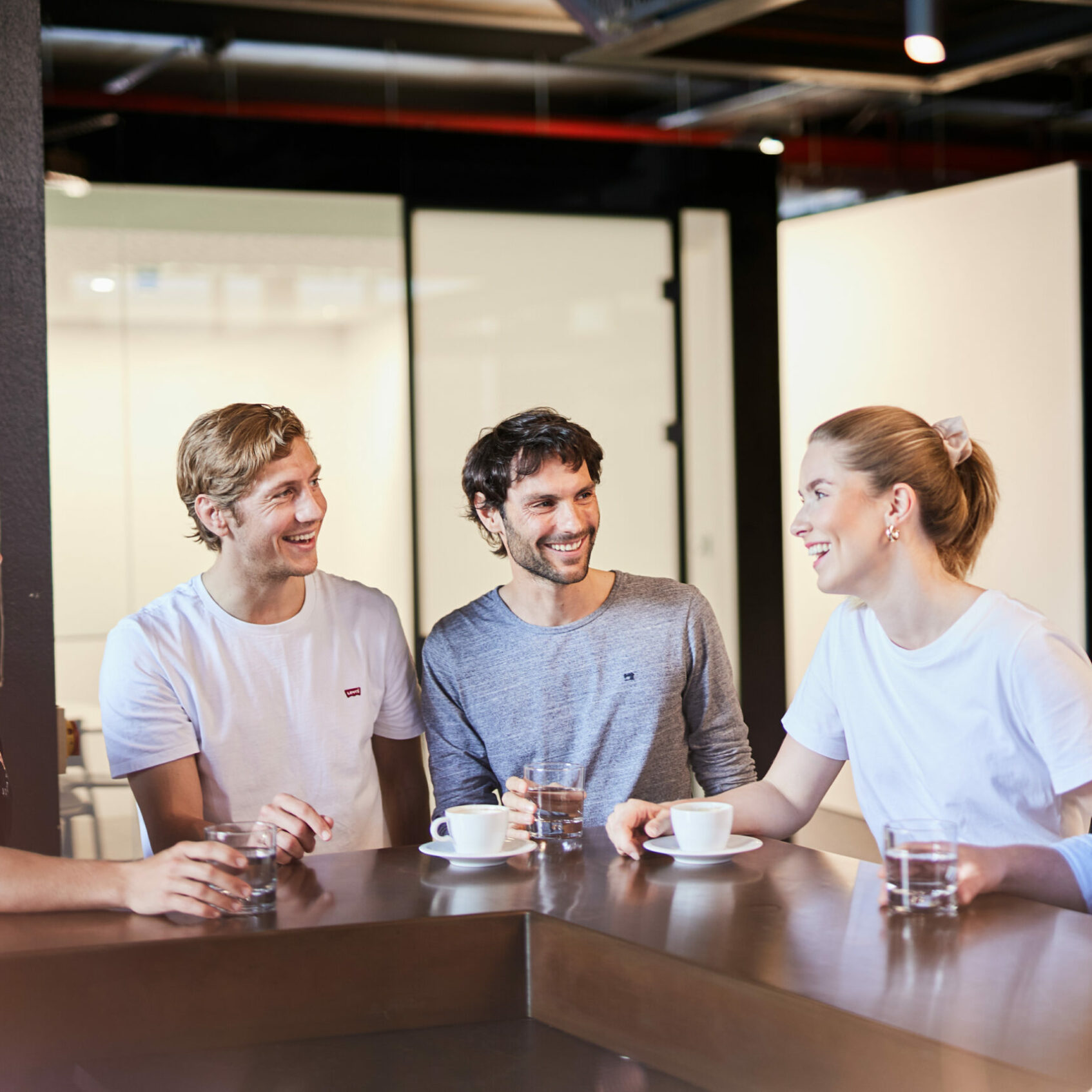 Five people standing at the office bar drinking coffee.