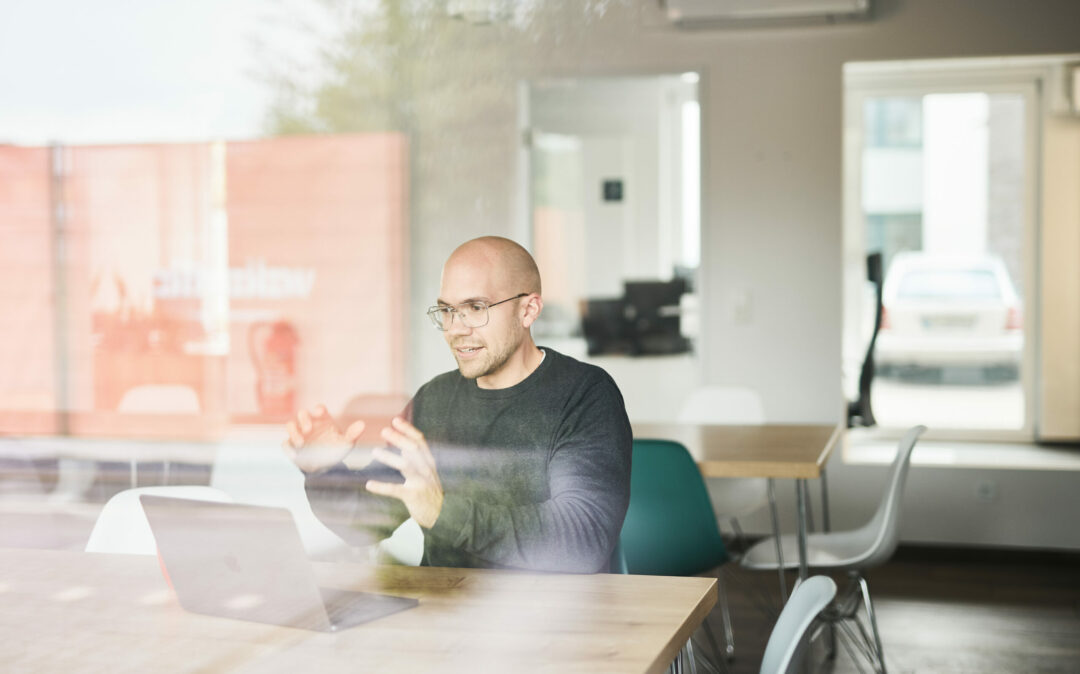 A man on a video call sitting in an empty meeting room.
