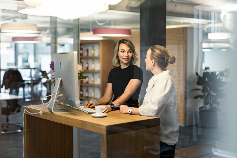 Zwei Frauen, die an einem Steharbeitsplatz miteinander sprechen