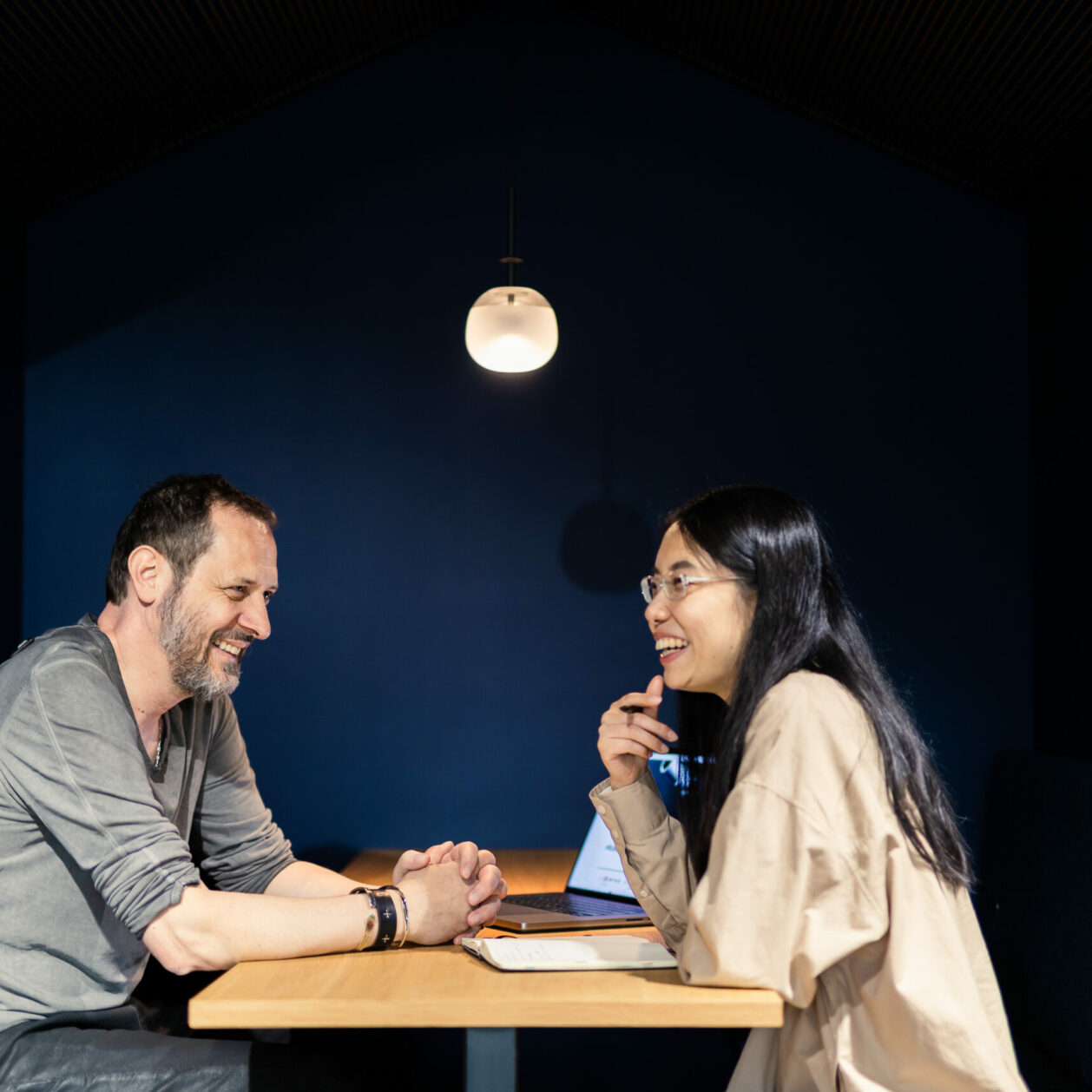 Foto von einem Mann und einer Frau, die sich in einer Sitzecke gegenüber sitzen und zusammen über etwas lachen.