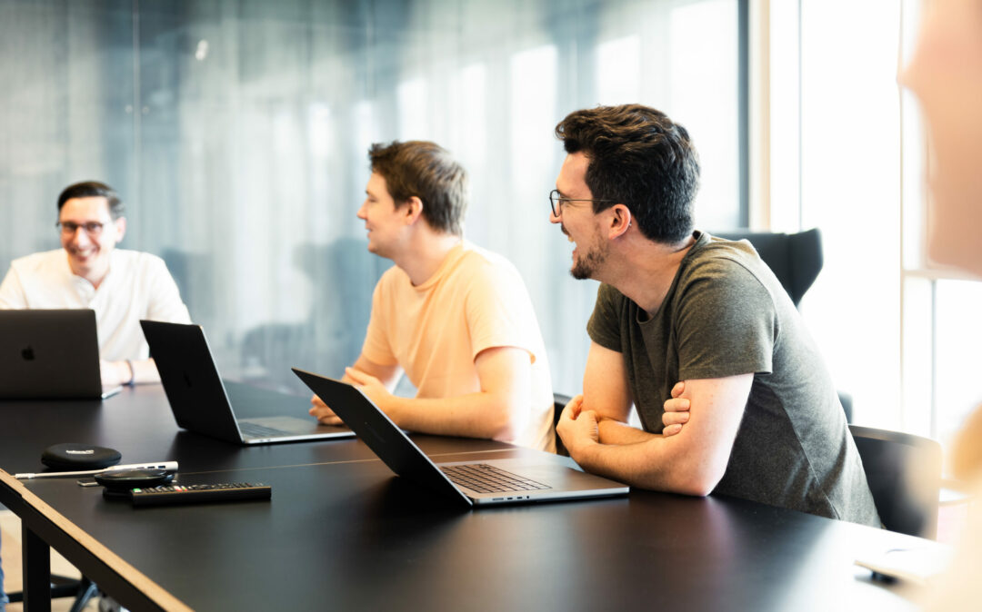 Drei Männer, die mit ihren Laptops an einem Konferenztisch sitzen.