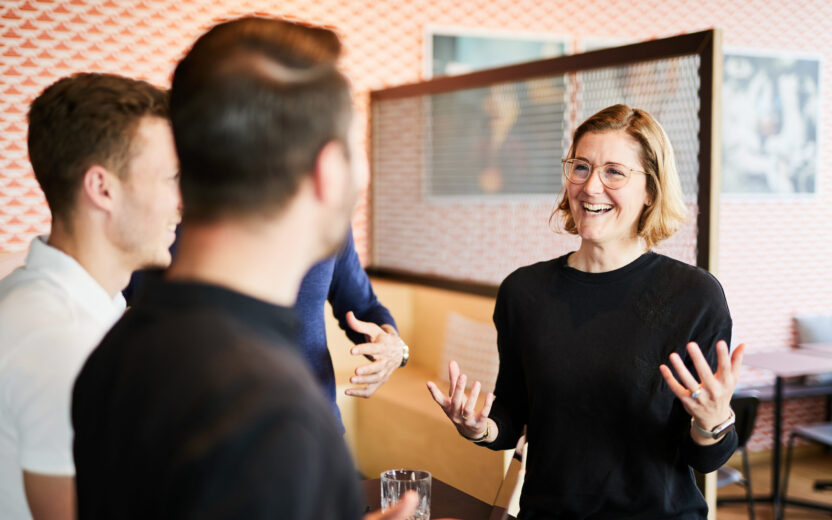 A woman talking to her three colleagues, gesturing with her hands.