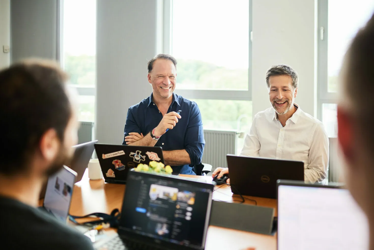 Photo of two men sitting in a meeting with their laptops.