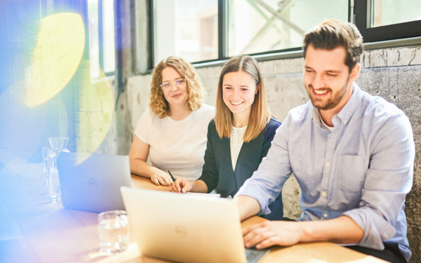 Drei Kollegen, die an einer Office-Bar sitzen und an einem Laptop arbeiten.