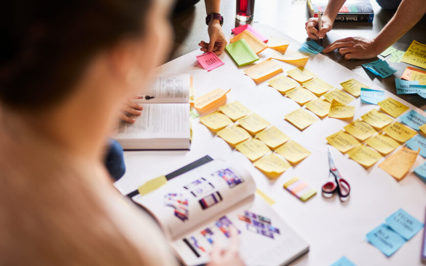 Mehrere Personen arbeiten in einem Workshop zusammen und sammeln Ideen auf Post-its auf einem großen Blatt Papier.