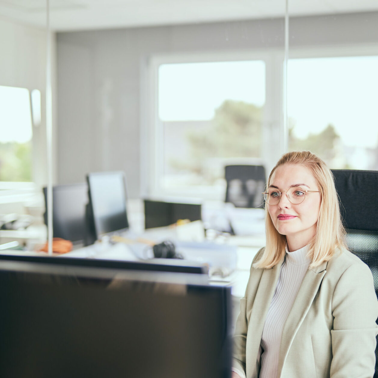 Foto von einer Frau, die an ihrem Büroarbeitsplatz sitzt und auf ihren Desktop schaut.