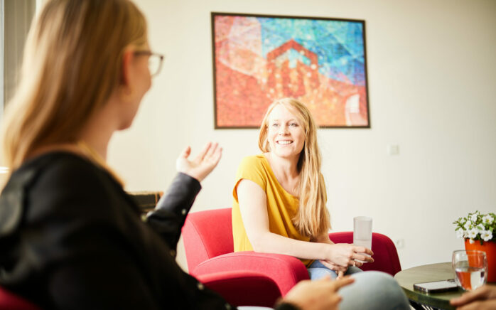 Photo of two young women sitting on armchairs having a friendly conversation.