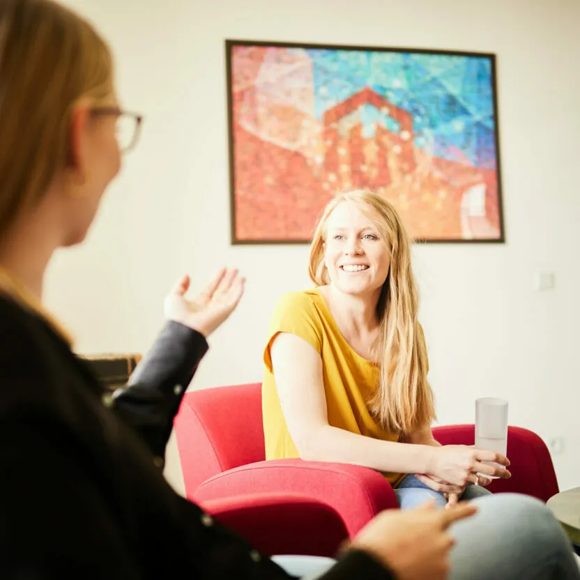Photo of two young women sitting on armchairs having a friendly conversation.