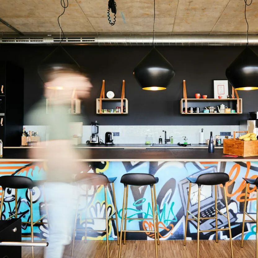 Bild von einer modernen Office-Küche mit Graffiti-Verzierung an der Barfront, wo gerade ein Mann vorbeiläuft.