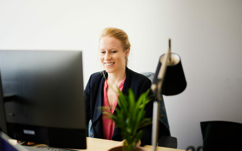 Foto von einer glücklichen Frau, die an ihrem Büroarbeitsplatz sitzt und arbeitet.