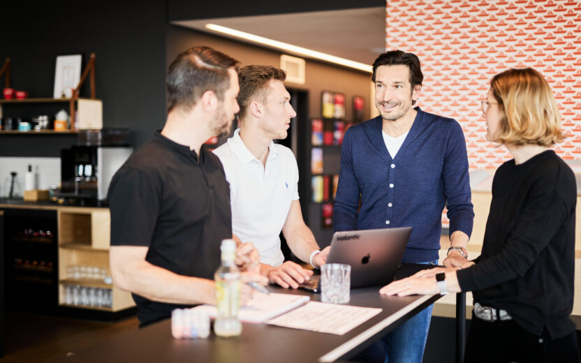 Photo of three colleagues having a meeting at a standing desk.