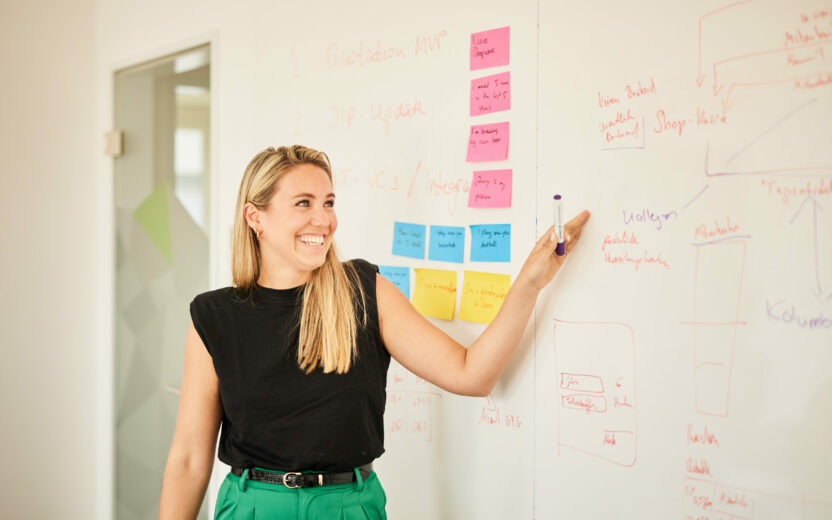 Photo of a woman explaining her strategy on a whiteboard.