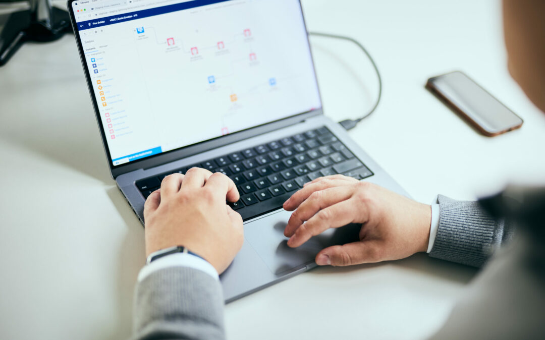 Photo of a man's hands resting on the keyboard of his laptop.