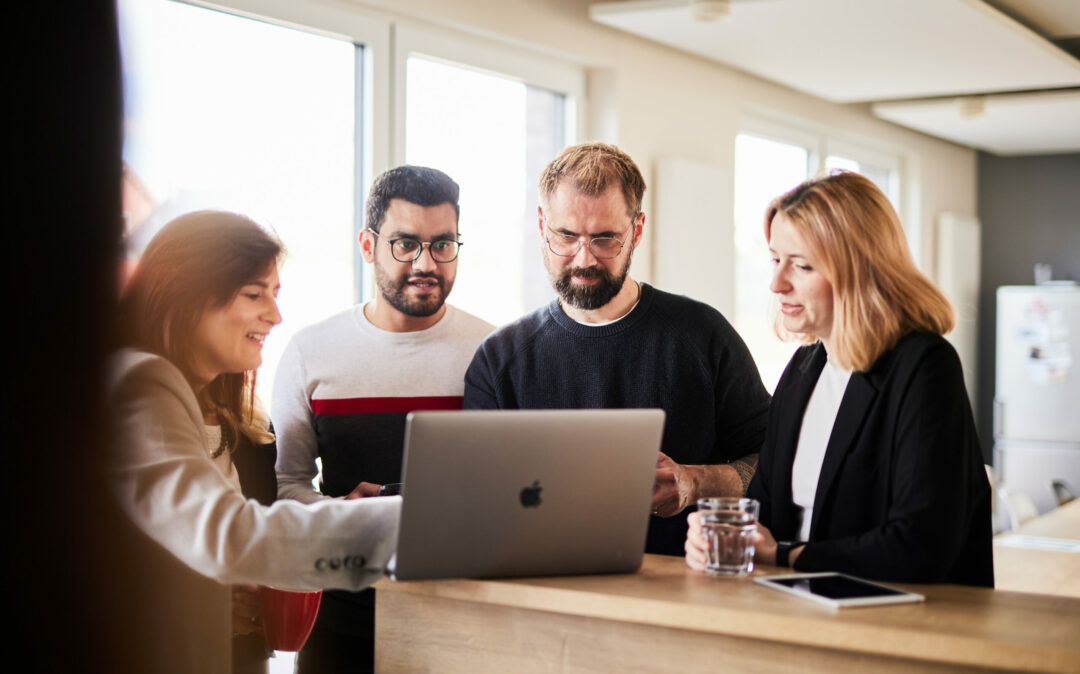 A group of colleagues looking at a laptop together and talking about a project.