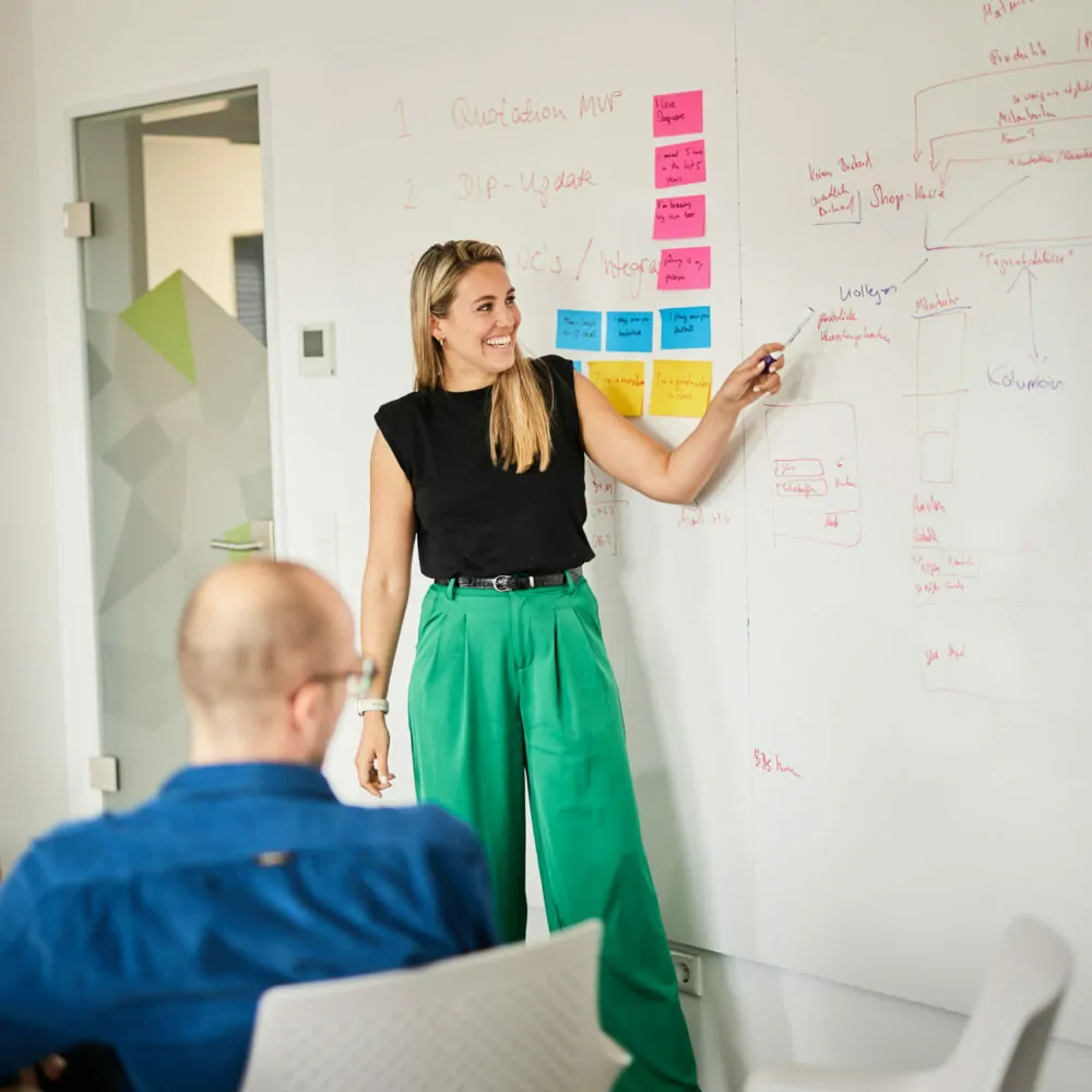 Photo of a woman standing at a whiteboard explaining a new strategy to her colleagues.