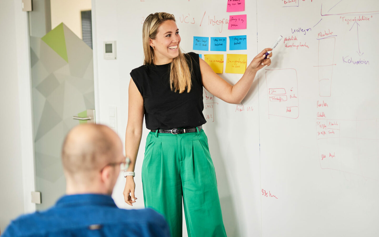 Photo of a woman standing at a whiteboard explaining a new strategy to her colleagues.