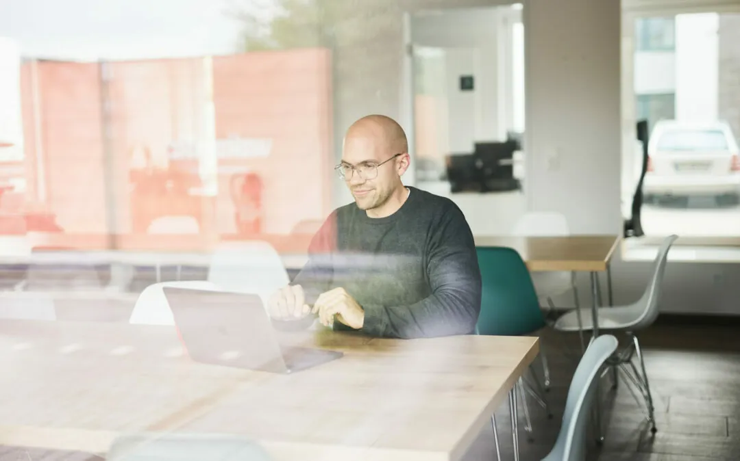 Photo of a smiling man in conference room listening to a presentation on his laptop.