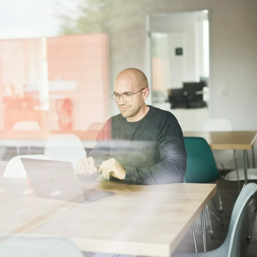 Photo of a smiling man in conference room listening to a presentation on his laptop.