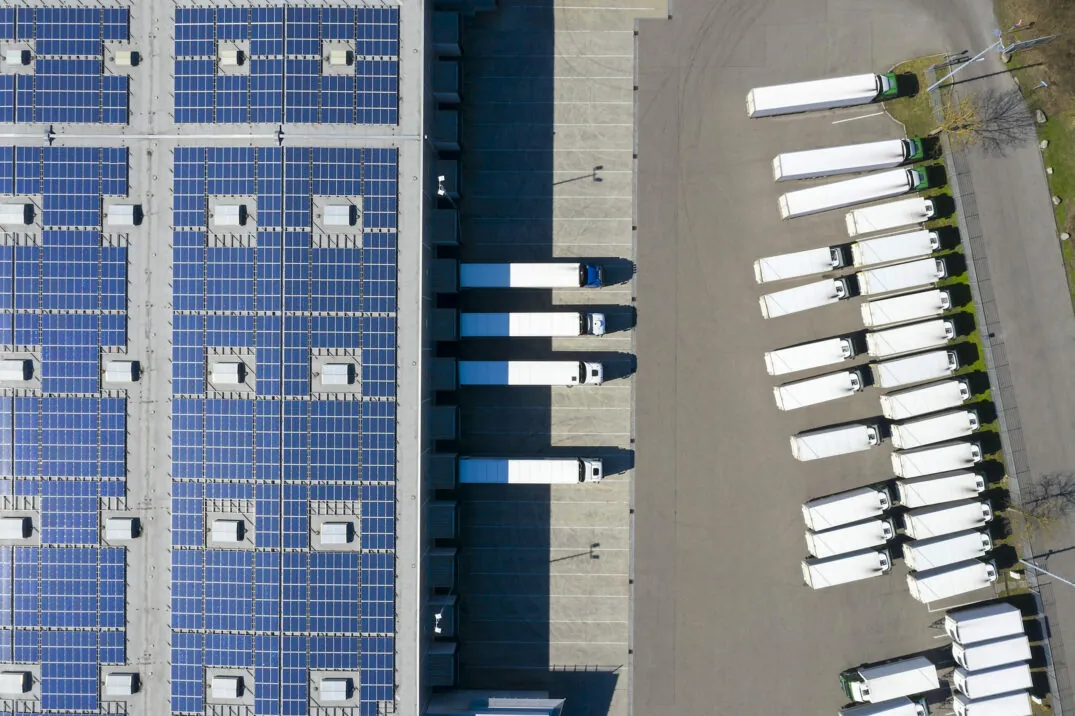 Luftaufnahme von LKWs, die im Logistikzentrum, Distributionslager mit Solar-Photovoltaik-Panels beladen werden