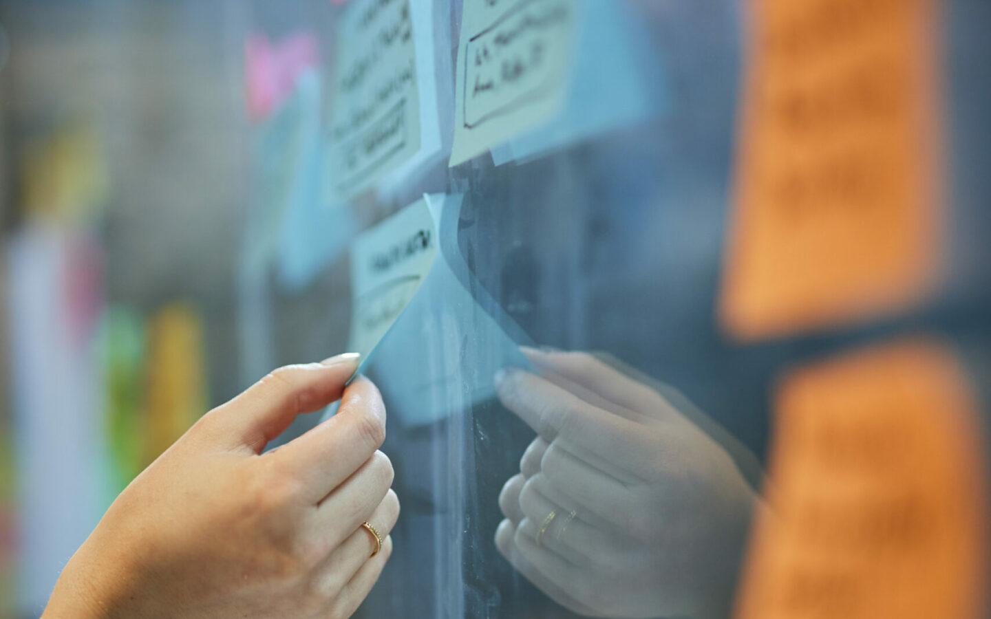 Image detail of a woman's hand taking a Post-It from a glass wall.